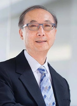 Professional portrait of an Asian man in a dark suit and blue striped tie, wearing glasses, smiling at the camera for a business profile.